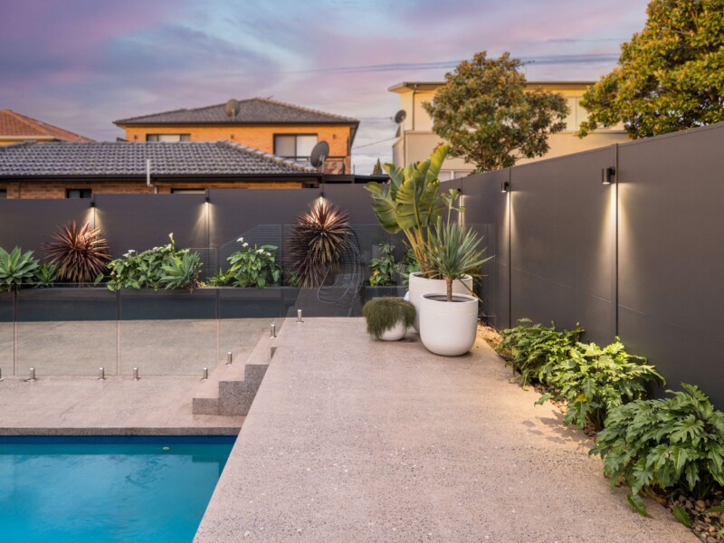Boundary wall and fencing project inspiration: SlimWall with aluminium posts and integrated lighting. The dark paint colour makes the foliage of the plants pop.