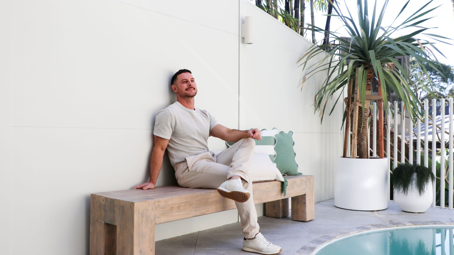 Darren Palmer sitting on a bench seat in his pool area with a ModularWalls TrendWall behind him